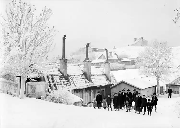 Vinterbild från Vita Bergen norrut. Vuxna och barn med kälke vid Lilla Mejtens Gränd 4. På berget i fonden byggdes Sofia kyrka 1903-1906.