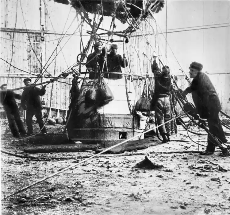 Någon minut före starten. I gondolen står Andrée längst till vänster, bredvid honom Strindberg. Mellan dem skymtar Fraenkels rygg och nacke.